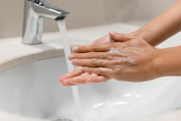 Person washing hands with soap under running water in a kitchen sink, emphasizing the importance of hygiene and food safety in meal preparation, especially for dishes like Kabsa in cloud kitchens.
