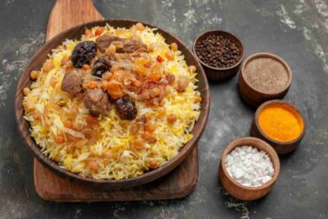 A steaming plate of Kabsa, a traditional Arabic rice dish, garnished with tender meat, raisins, and aromatic spices like black pepper, turmeric, and saffron, served in a rustic wooden bowl—perfect for winter warmth and rich in nutritional value.
